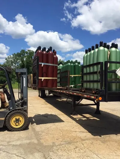 Forklift loading pallets of high-pressure gas cylinders onto a flatbed delivery trailer at Northeast Gas & Ice