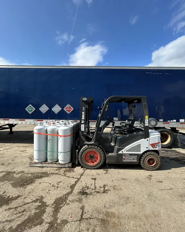 Forklift staging gas cylinders next to a Northeast Gas & Ice delivery trailer in New England