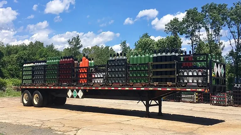 Northeast Gas & Ice flatbed trailer fully loaded with mixed industrial gas cylinder racks — oxygen, argon, nitrogen, and specialty gases ready for delivery
